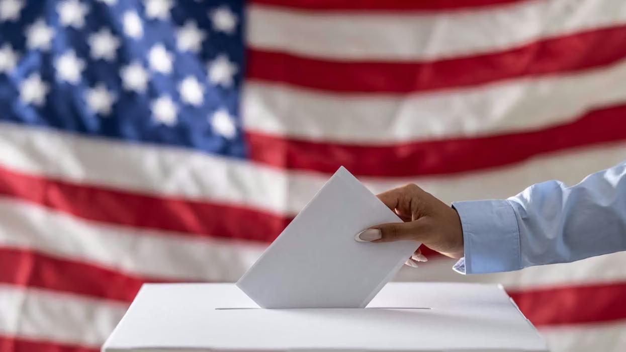 hand-placing-a-ballot-into-a-box-with-american-flag-in-the-background.avif